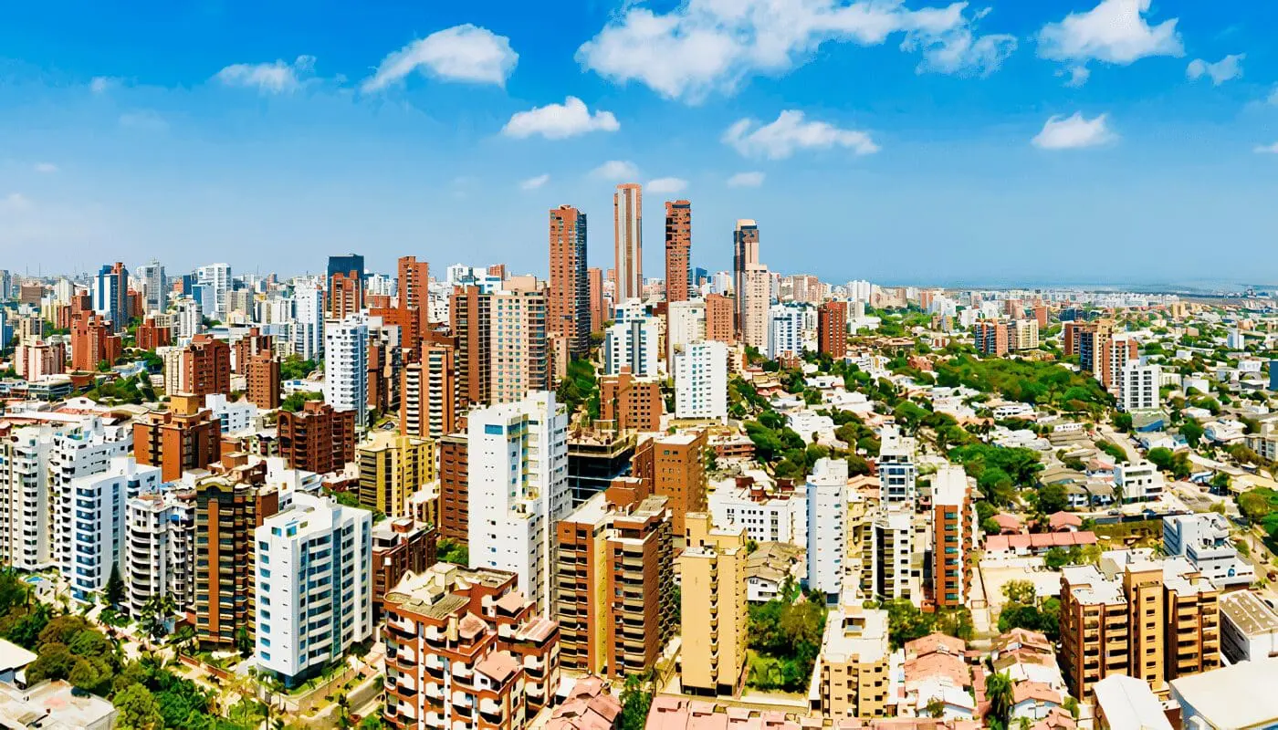 Vista aérea de Barranquilla, Colombia, con un horizonte lleno de coloridos edificios altos, abundante vegetación y un cielo azul despejado que enmarca la costa Caribe.